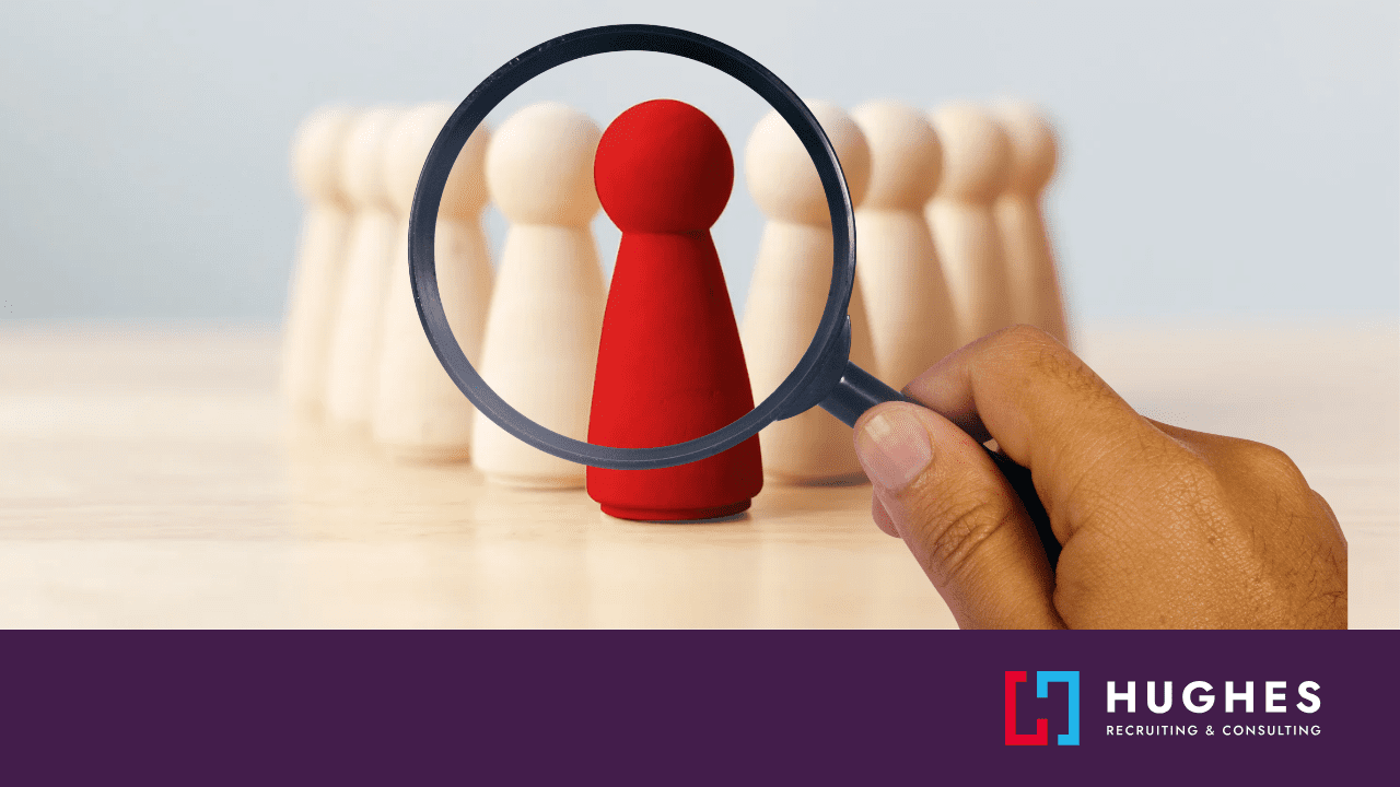 Wooden figures stand in a V formation, with a red figure at the tip. A magnifying glass focuses on the red figure.